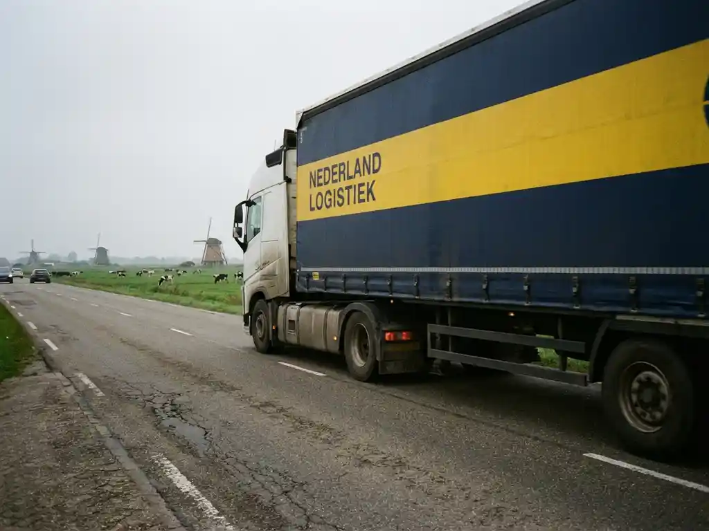 Grote vrachtwagen met donkerblauwe en gele huisstijl rijdt over Nederlandse snelweg met groene velden op achtergrond
