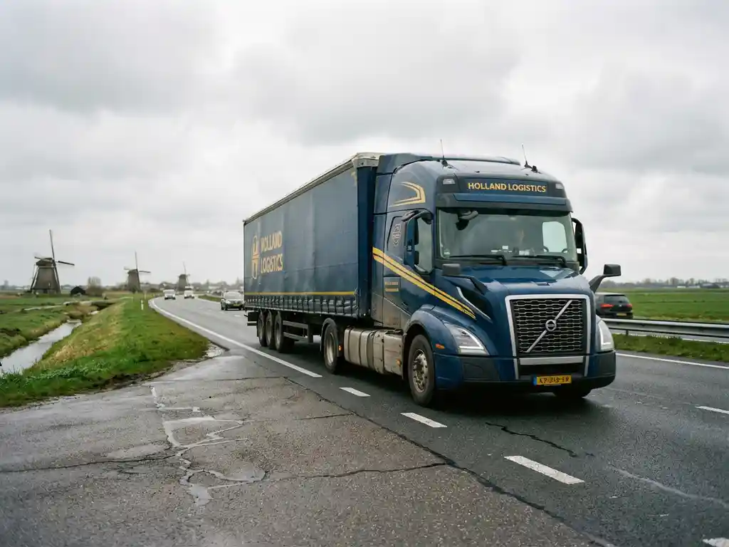 Grote vrachtwagen met donkerblauwe trailer en gele accenten rijdt over Nederlandse snelweg door vlak landschap