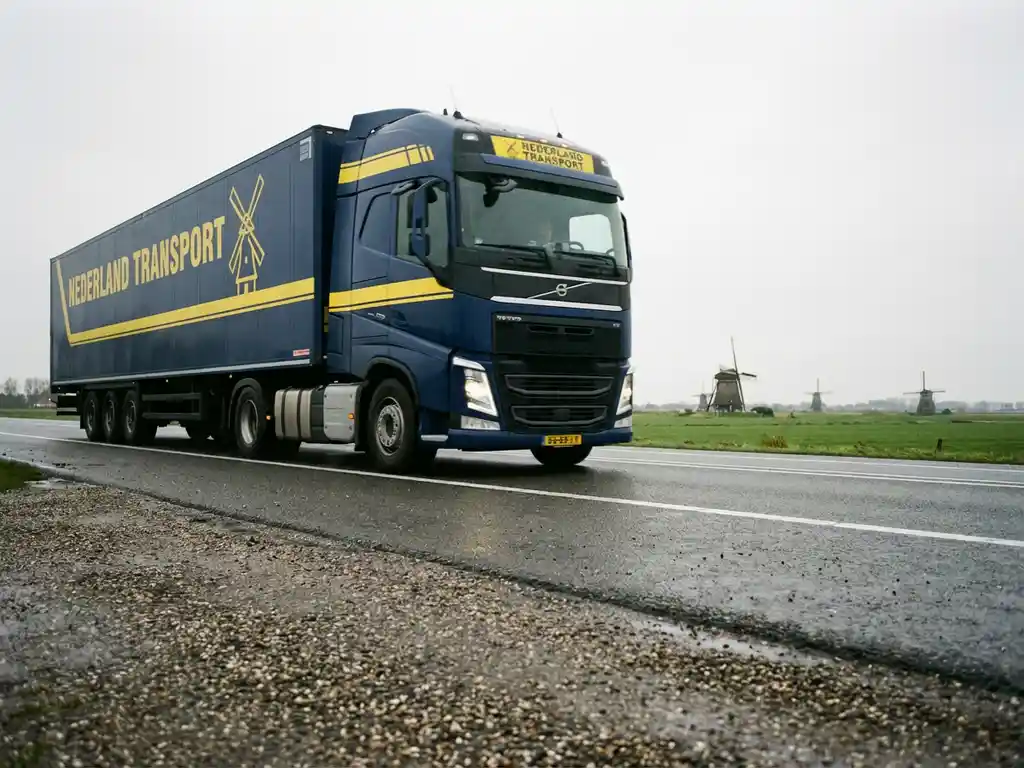 Grote vrachtwagen met donkerblauwe trailer rijdt over Nederlandse snelweg met groene velden en windmolens op achtergrond