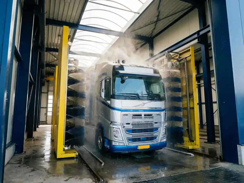 Europese vrachtwagen wordt gewassen in moderne wasstraat met roterende borstels en hogedrukspuiten